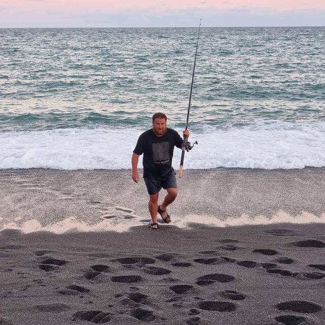 Man walking up the beach at sunset carrying a fishing rod
