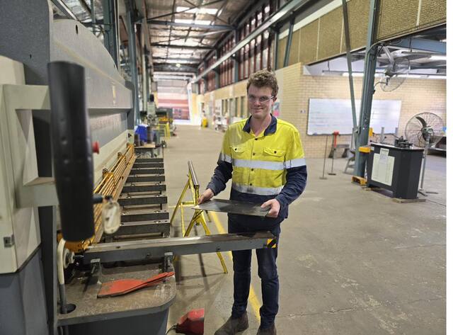 Young man in hi-vis and safety glasses holding sheet metal in a workshop
