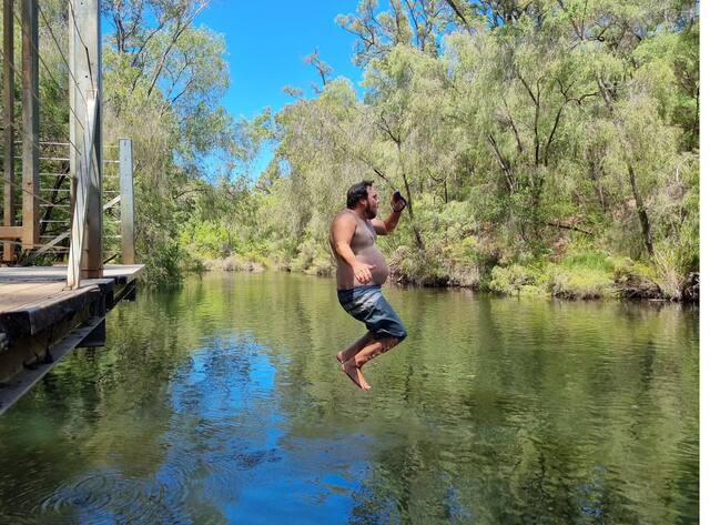 Man mid-air jumping from a bridge into a calm river surrounded by bush