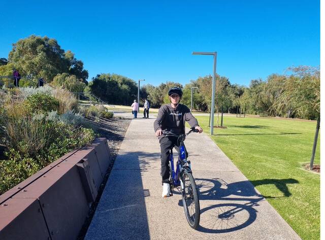 Man in a helmet riding a blue bike along a park path