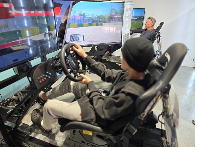 Person driving a racing simulator with a steering wheel and big screens